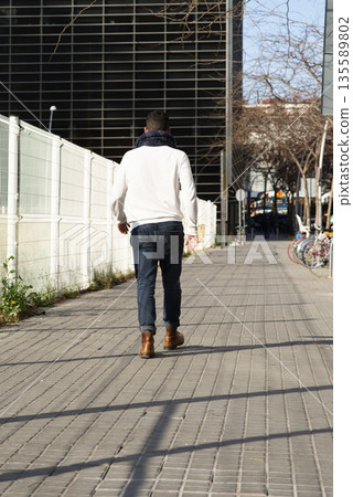 Young caucasian man walking away on urban sidewalk 135589802