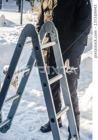 Man preparing a multi-position ladder for work in the snow. 135589943