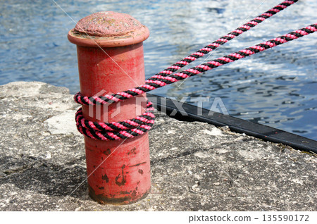 Red sailing hawser mooring rope from yacht in the port on concrete quay 135590172
