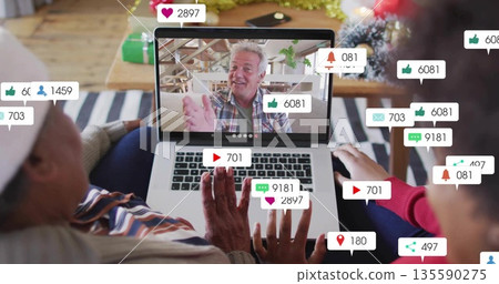 Family members waving at laptop screen in cozy living room, with gift boxes and notifications 135590275