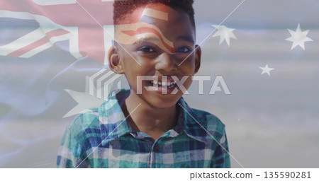 Smiling boy wearing green blue plaid shirt standing at shoreline, showing Australian flag overlay 135590281