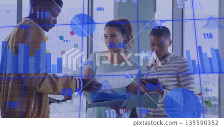 Collaborating colleagues reviewing reports and data charts in glass office with tablet smartphone 135590352