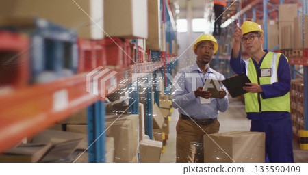 Scanning cardboard boxes on metal racks in warehouse aisle, men using tablet clipboard with helmets Scanning cardboard boxes on metal racks in warehouse aisle, men using tablet clipboard with helmets 135590409