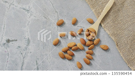 Arranging raw almonds on light grey countertop, with wooden spoon on burlap fabric, copy space Arranging raw almonds on light grey countertop, with wooden spoon on burlap fabric, copy space 135590454
