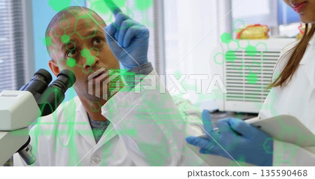 Pointing scientist in lab coat at green molecular overlay at lab bench with microscope, copy space Pointing scientist in lab coat at green molecular overlay at lab bench with microscope, copy space 135590468