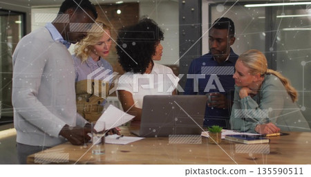 Colleagues gathering around laptop and documents in conference room, with network graphics 135590511