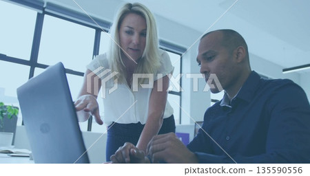 Collaborating colleagues wearing office attire pointing, typing on laptop in office with monitor 135590556
