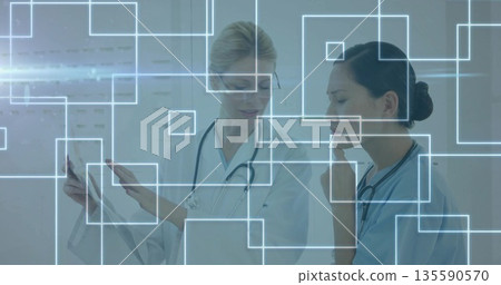 Studying medical chart and viewing digital overlays, doctors wearing scrubs, lab coat in clinic 135590570
