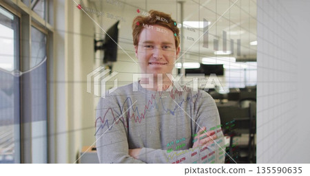 Standing analyst in gray sweater behind transparent panel in modern office, with financial charts 135590635