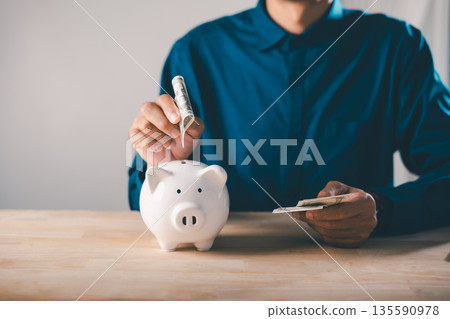 Global economy money bank piggy finance stock growth business concept illustrates man inserting cash into white piggy bank to save and invest economic assets and personal wealth Global economy money bank piggy finance stock growth business concept illustrates man inserting cash into white piggy bank to save and invest economic assets and personal wealth 135590978