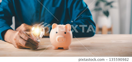 Financial innovation idea uses piggy bank money energy investment save retirement, man holding glowing light bulb represents smart strategy for wealth saving and finance growth 135590982