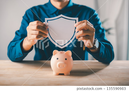 Businessman holding shield over piggy bank to protect money save plan financial finance insurance saving, ensuring security for personal wealth and future investment strategies 135590983
