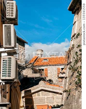 terracotta tiled rooftop with chimneys and ducts, city skyline behind sunlit building with vents and cables 135591559