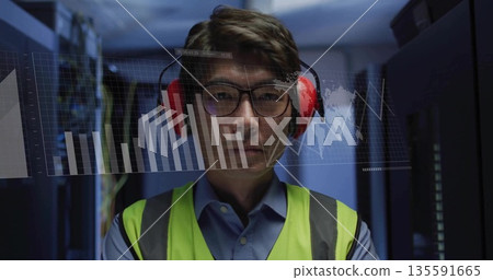 Operating servers and monitoring data charts, data center technician in yellow vest and headphones 135591665