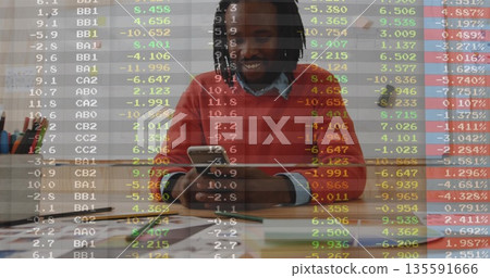 Smiling man wearing orange sweater using smartphone in office with chart board, stock data overlay 135591666