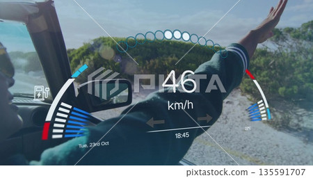 Driving Indian woman wearing dark jacket extending arm outside convertible on coastal road with HUD 135591707