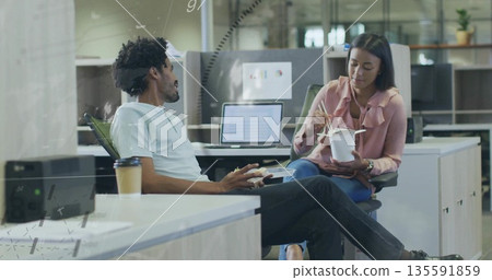 Sharing lunch, colleagues eating sandwich and using chopsticks on takeaway container in open office 135591859