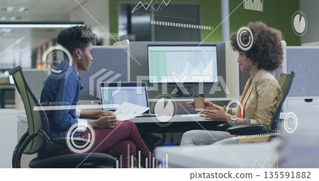 Reviewing charts, colleagues discussing graphs at open-plan office desk with laptop and coffee cup Reviewing charts, colleagues discussing graphs at open-plan office desk with laptop and coffee cup 135591882