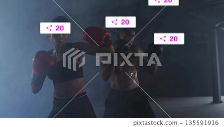 Sparring adult woman and man maintaining stances in dark hazy gym, with red, black boxing gloves Sparring adult woman and man maintaining stances in dark hazy gym, with red, black boxing gloves 135591916