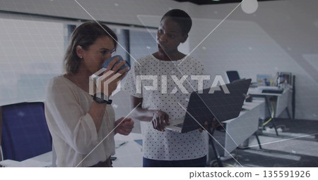 Two colleagues in business attire discussing laptop screen in modern office, with blue coffee mug 135591926