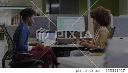 Two women in business attire collaborating over printed documents and coffee at open plan office Two women in business attire collaborating over printed documents and coffee at open plan office 135591927