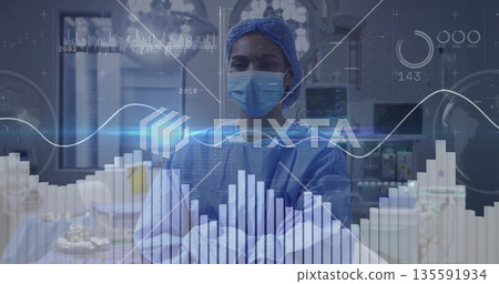 Standing female surgeon in surgical attire crossing arms in OR, with data overlays on monitors Standing female surgeon in surgical attire crossing arms in OR, with data overlays on monitors 135591934