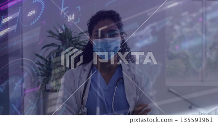 Standing female doctor folding arms wearing mask and stethoscope in clinic, with digital overlays Standing female doctor folding arms wearing mask and stethoscope in clinic, with digital overlays 135591961