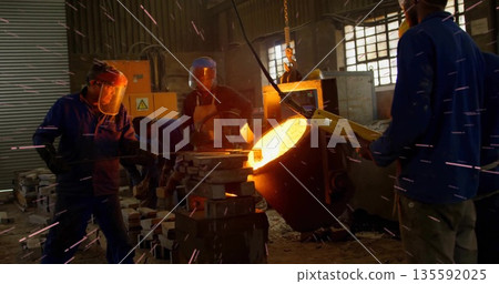 Pouring workers guiding molten metal from ladle in foundry shop with hoist chain molds face shields Pouring workers guiding molten metal from ladle in foundry shop with hoist chain molds face shields 135592025