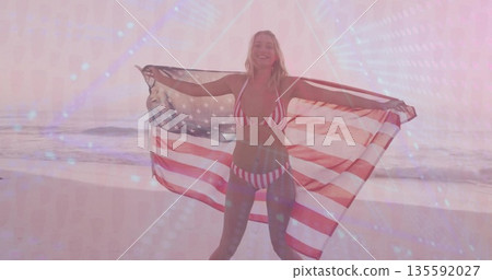 Standing woman holding American flag behind back on sandy shoreline at sunrise, with striped bikini Standing woman holding American flag behind back on sandy shoreline at sunrise, with striped bikini 135592027