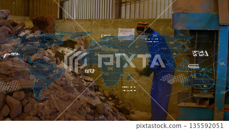 Shoveling worker in coverall feeding rocks into press in workshop, with map overlay, copy space 135592051