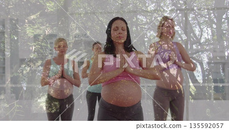 Four pregnant women wearing sportswear holding prayer pose in yoga studio, with yoga mats 135592057