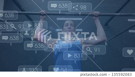 Woman in blue tank top doing pull-up in gym, with floating social media notification icons Woman in blue tank top doing pull-up in gym, with floating social media notification icons 135592083