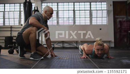 Performing push-up mid adult female client training with male coach at gym, with kettlebells 135592171