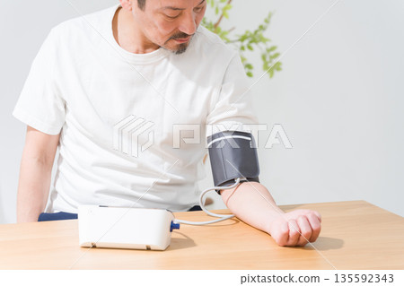 Middle-aged man measuring blood pressure with a sphygmomanometer 135592343