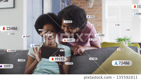 Leaning over gray sofa mother and daughter using tablet in living room, notification icons 135592811