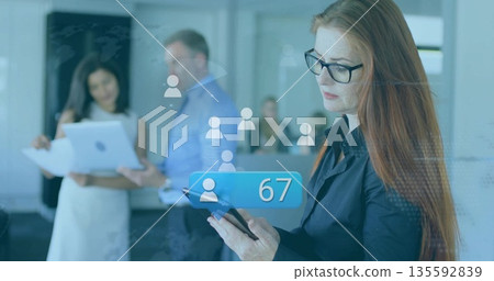 Red-haired woman in black blouse reading tablet in office, with icons, blue badge, copy space 135592839
