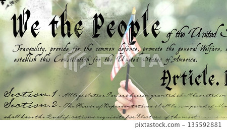 Child hand grasping US flag stick before blurred foliage, overlaying Constitution text, copy space 135592881