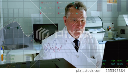 Senior scientist wearing lab coat and tie analyzing real-time data on monitors in lab, with sink 135592884
