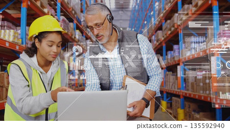 Warehouse team reviewing inventory on laptop at mobile workstation, with neon vest and hardhat 135592940