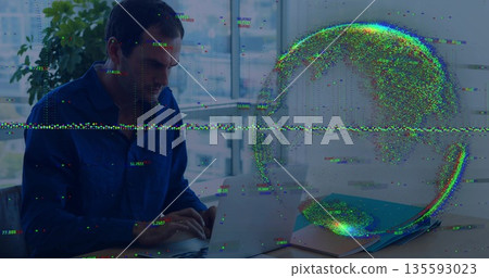 Man wearing blue shirt reviewing laptop at office desk, with notebook pen plant and globe glitch 135593023