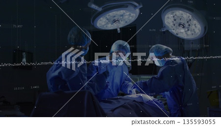 Three surgeons wearing scrubs performing surgery on patient in OR, with overhead lights and monitor Three surgeons wearing scrubs performing surgery on patient in OR, with overhead lights and monitor 135593055
