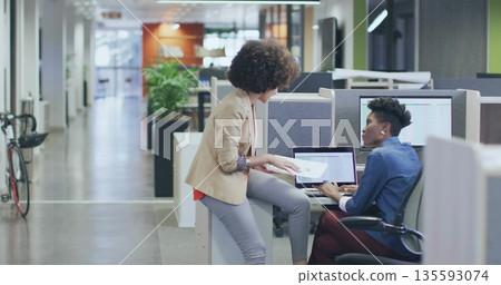 Reviewing documents and using laptops, coworkers wearing blazers working in office, with bicycle Reviewing documents and using laptops, coworkers wearing blazers working in office, with bicycle 135593074
