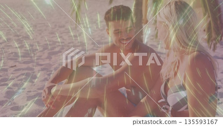 Smiling couple wearing swimwear chatting on tropical beach sand, with palm trunk and fronds shading Smiling couple wearing swimwear chatting on tropical beach sand, with palm trunk and fronds shading 135593167