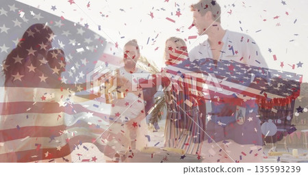 Raising group of friends clinking beer bottles on outdoor patio, with confetti and grill station 135593239