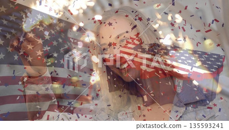 Snapping woman holding smartphone in room, star-shaped confetti, US flag overlay, string lights Snapping woman holding smartphone in room, star-shaped confetti, US flag overlay, string lights 135593241