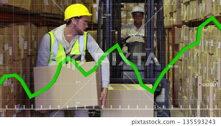 Worker in yellow helmet, safety vest lifting cardboard box in warehouse with forklift, green graph 135593243