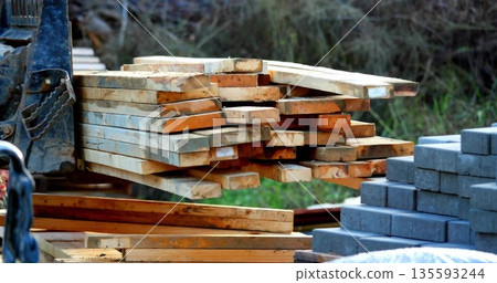 Lifting plank bundle using forklift mounting plate and chain at storage yard, with concrete blocks Lifting plank bundle using forklift mounting plate and chain at storage yard, with concrete blocks 135593244