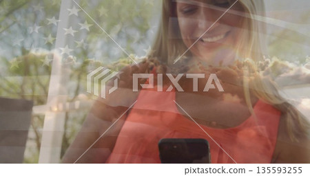Holding woman wearing coral top smiling at smartphone on backyard porch deck, with flag overlay Holding woman wearing coral top smiling at smartphone on backyard porch deck, with flag overlay 135593255