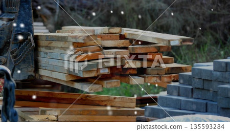 Forklift forks supporting pile of planks near stacked blocks in supply yard, snowflakes falling 135593284