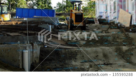Operating road roller compactor smoothing dirt at construction site, with footings, PVC pipes Operating road roller compactor smoothing dirt at construction site, with footings, PVC pipes 135593288